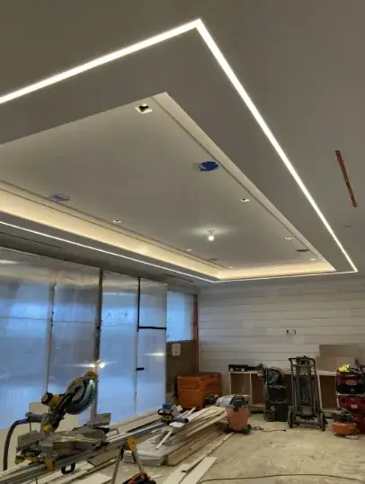 Two-step tray ceiling with a continuous linear LED channel glowing around each step, in a room still under renovation with a mitre saw and materials on the floor
