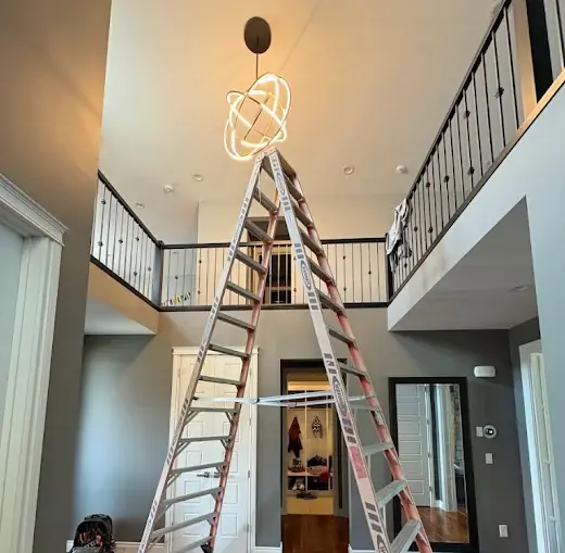 Extension ladder in a two-storey foyer under a newly hung orbital LED pendant light