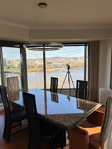 Ring LED pendant over a stone dining table in a condo with floor-to-ceiling windows and a river view